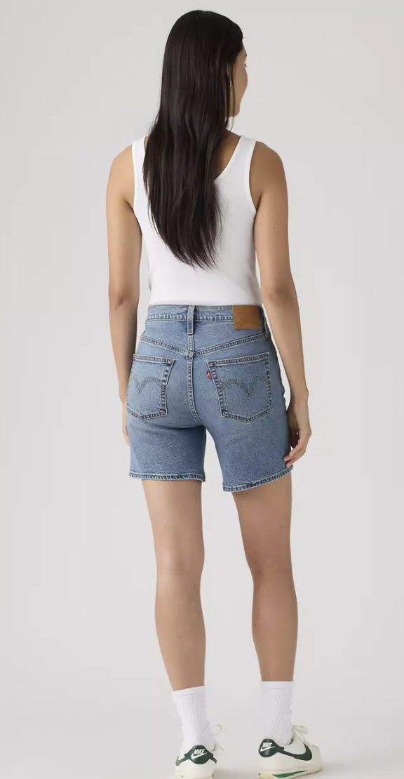 Person wearing a white tank top and Levi's blue denim shorts on a plain background