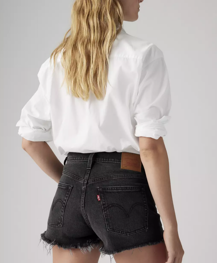 Person wearing a white shirt and black Levi's shorts on a plain background