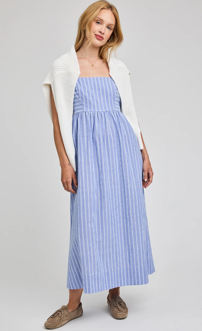 Woman wearing a blue striped dress with a white cardigan on a gray background
