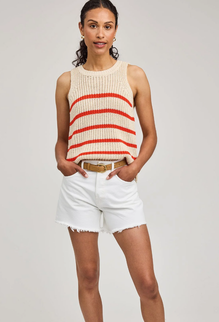 Woman wearing a sleeveless grenadine and white striped top with white shorts on a plain background