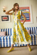 Woman in a yellow floral dress standing in a room with a striped couch and framed pictures on the wall.