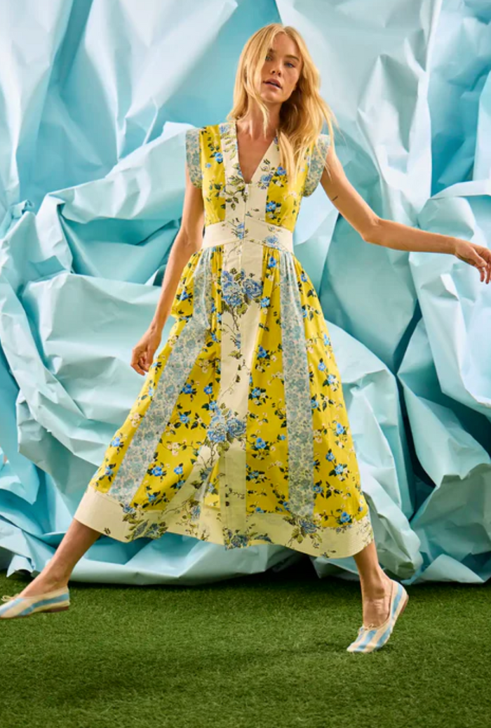 Woman in a yellow floral dress standing against a blue fabric background