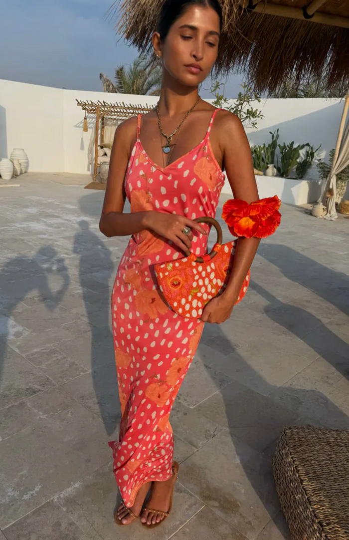 Woman in a colorful dress holding a red clutch in an outdoor setting.
