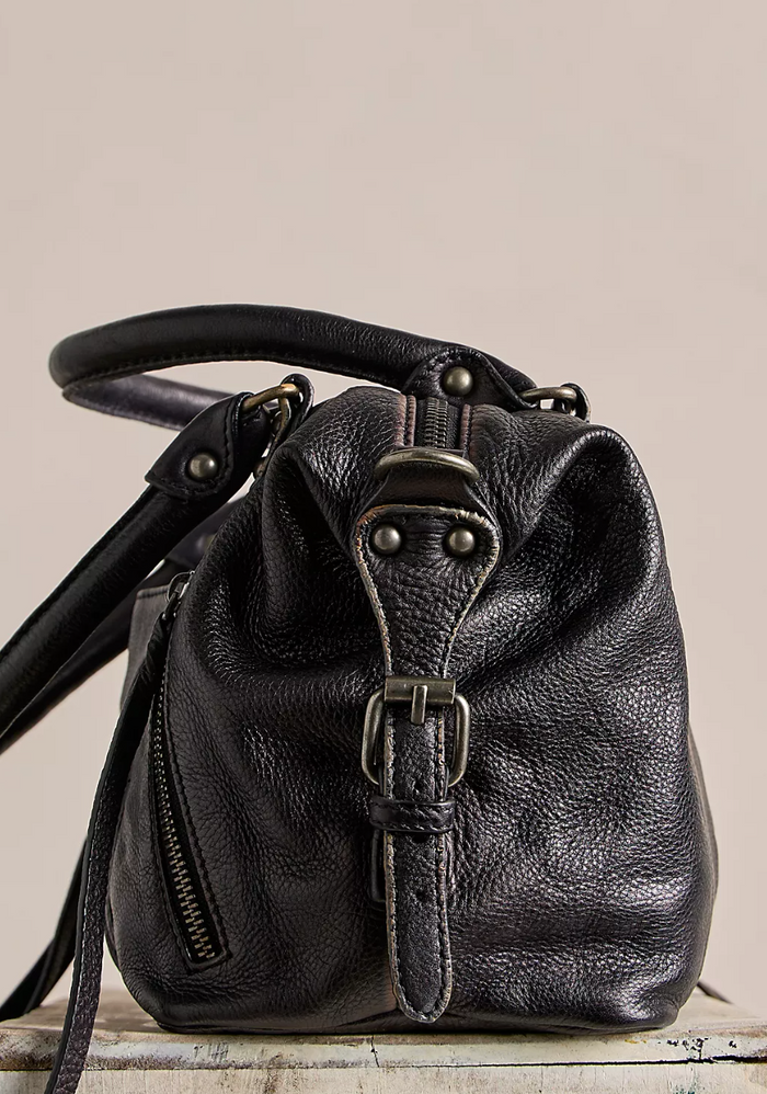 Black leather handbag with a strap on a beige background, side view