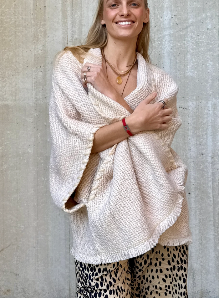 Woman wearing a beige knitted shawl against a concrete wall