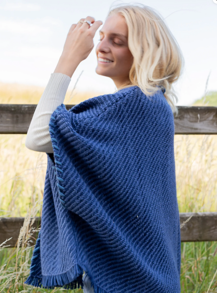 Woman wearing a blue knitted poncho in an outdoor setting