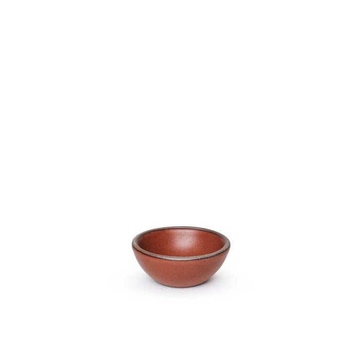 A tiny rounded ceramic bowl in a cool burnt terracotta color featuring iron speckles and an unglazed rim