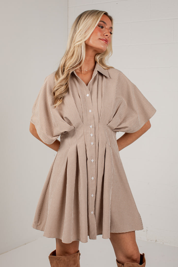 A woman modeling a beige and white striped short-sleeve button-up dress with a flared skirt, paired with brown boots, against a white studio background.