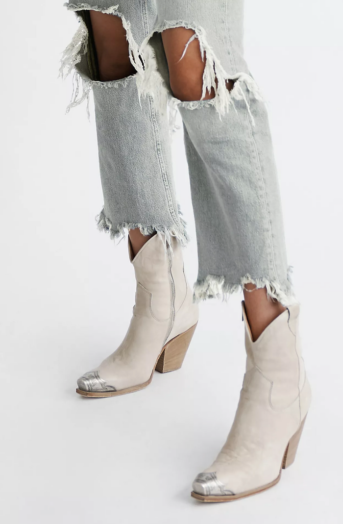Bone cowboy boots worn with ripped light blue jeans on a white background