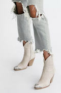 Bone cowboy boots worn with ripped light blue jeans on a white background