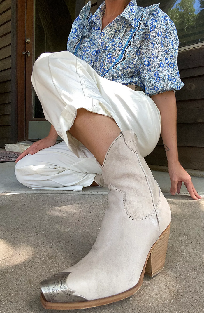 Person wearing bone western boots with metallic toes, sitting on a step.