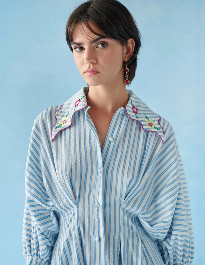 Woman wearing a blue and white striped shirt with floral embroidery on a light blue background