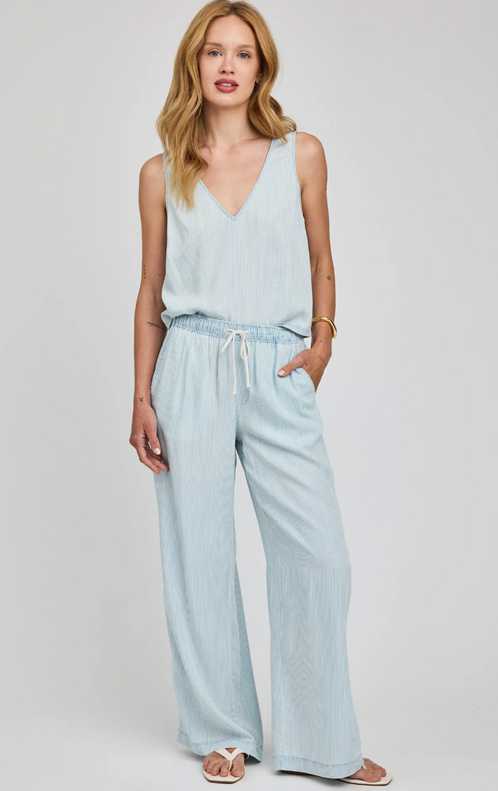 Woman wearing a light blue sleeveless top and wide-leg pants on a plain background
