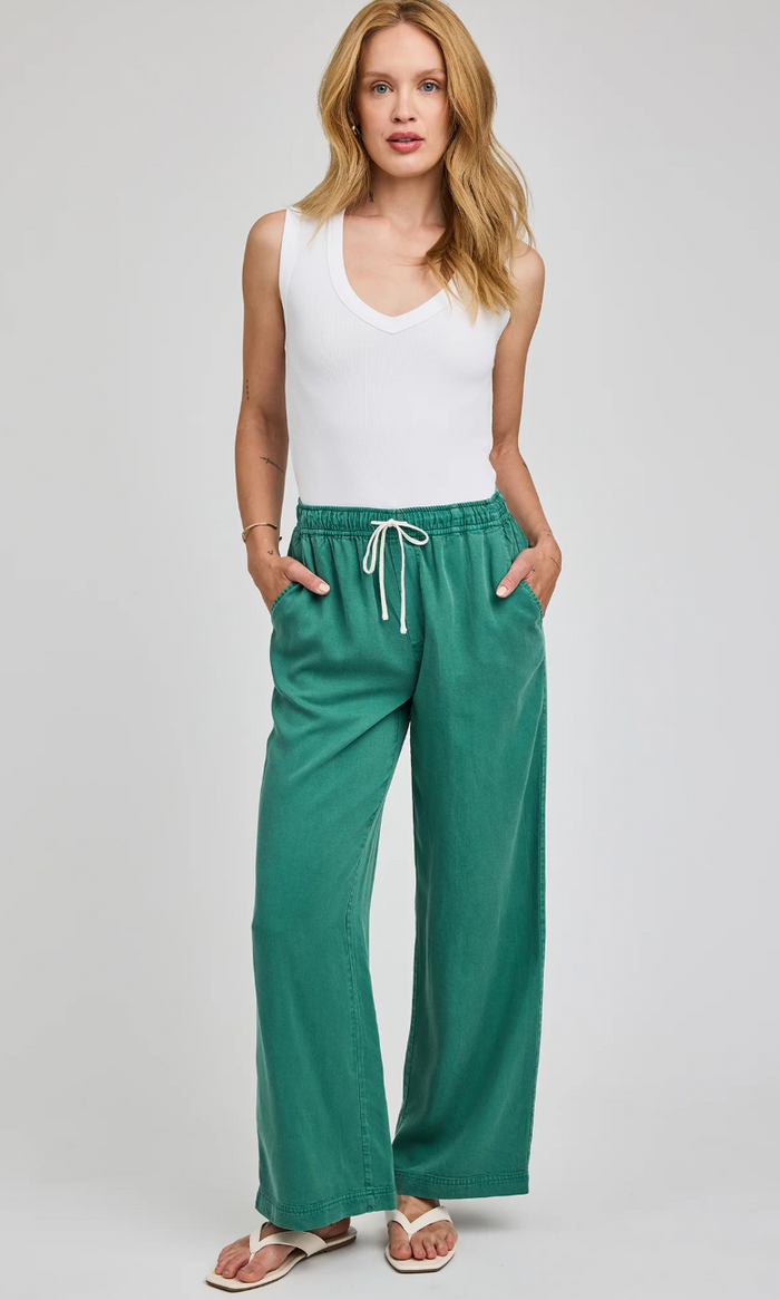 Woman wearing a white sleeveless top and green pants on a gray background