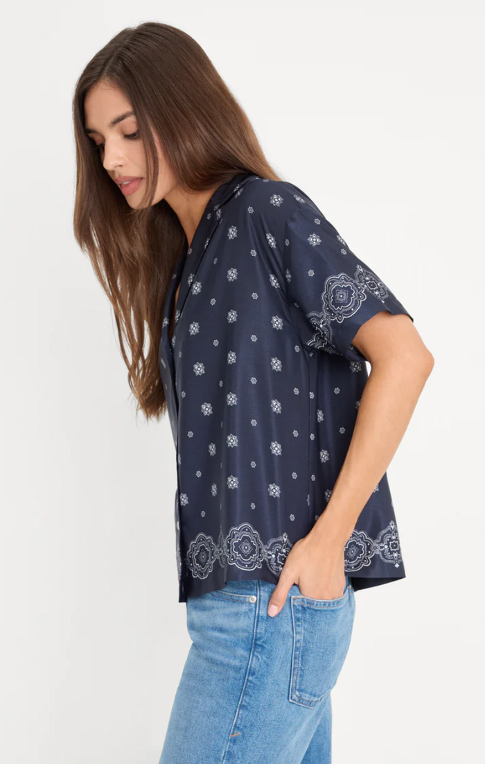 Woman wearing a navy blue patterned shirt and blue jeans on a white background