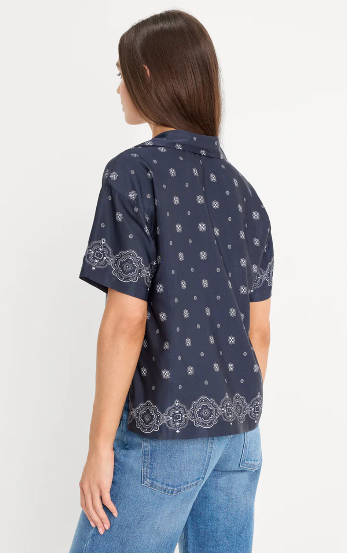 Person wearing a navy blue patterned shirt and jeans on a white background