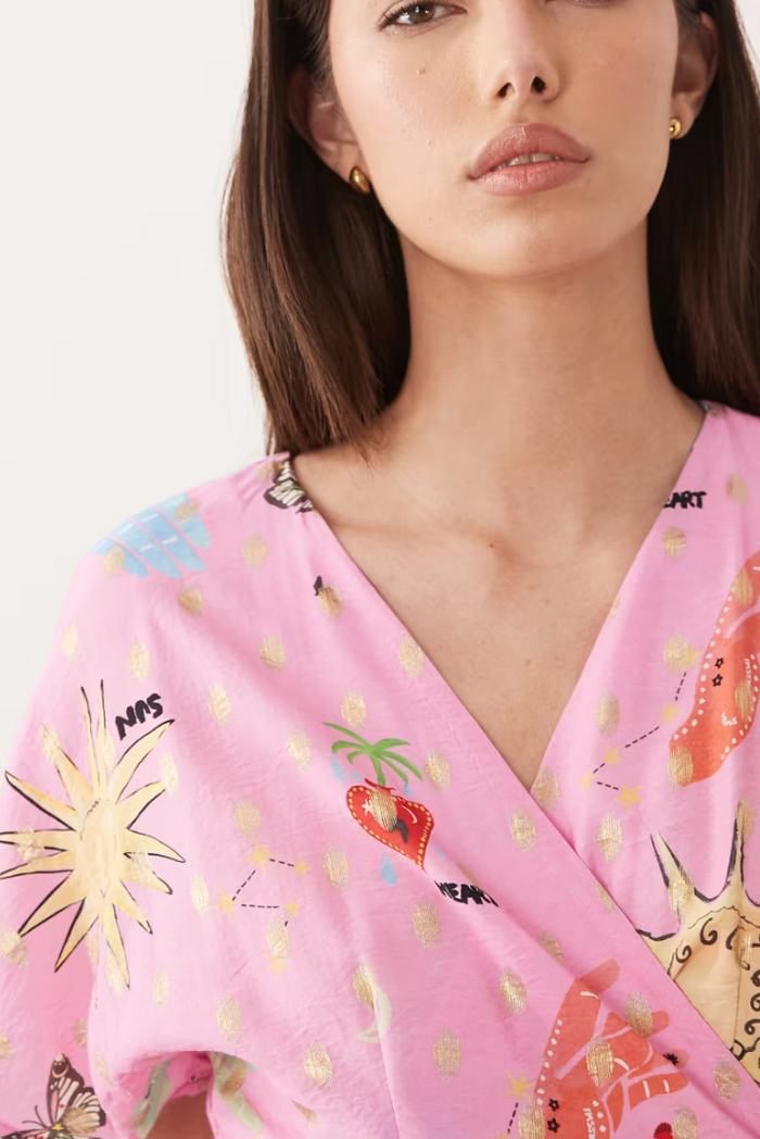 Woman wearing a pink patterned top with colorful designs.