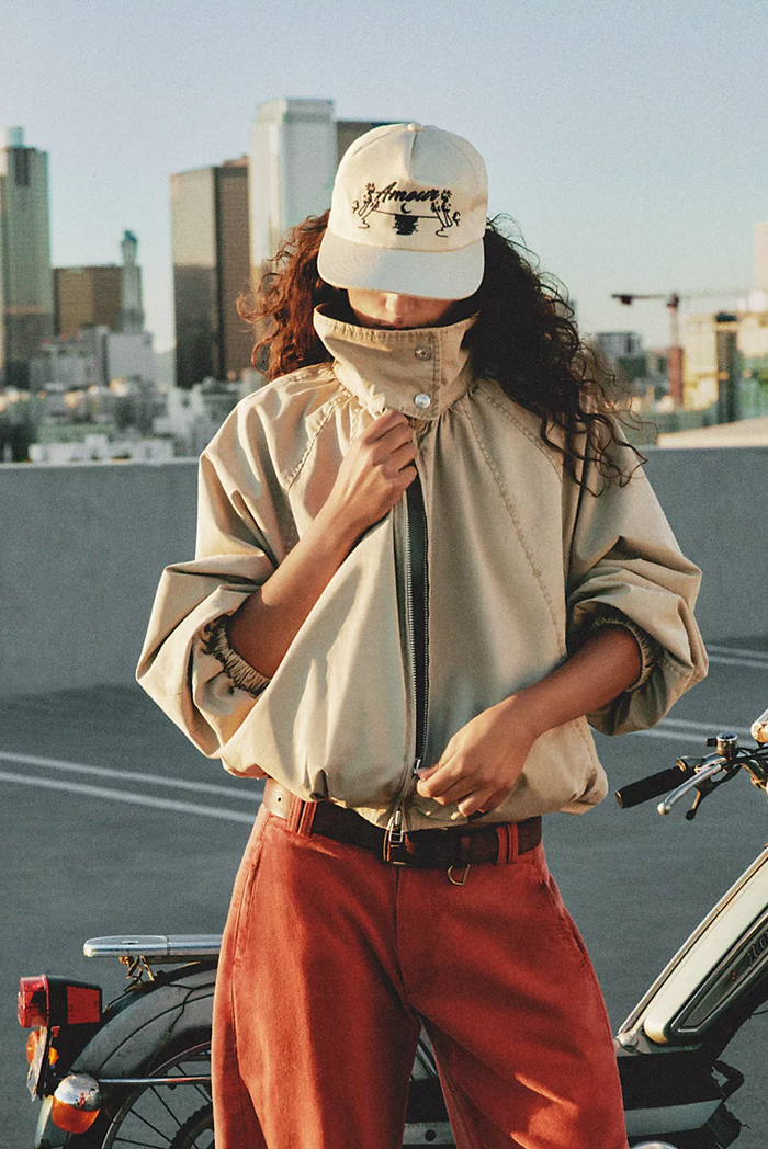 Person wearing a beige jacket and red pants with a cityscape background
