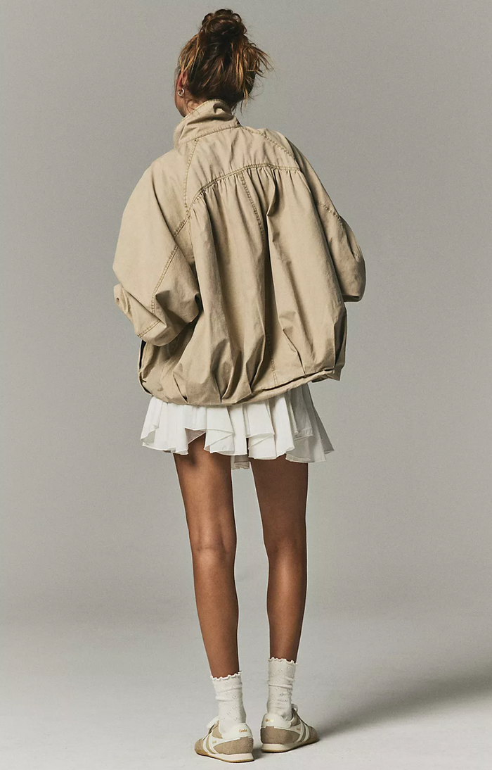 Person wearing a beige jacket and white skirt on a plain background