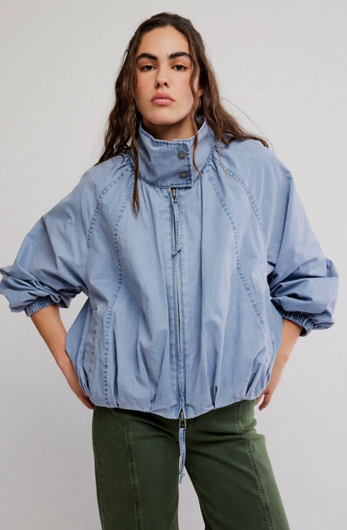Woman wearing a light blue jacket and green pants against a plain background