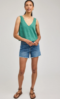 Woman wearing a green sleeveless top and denim shorts on a plain background