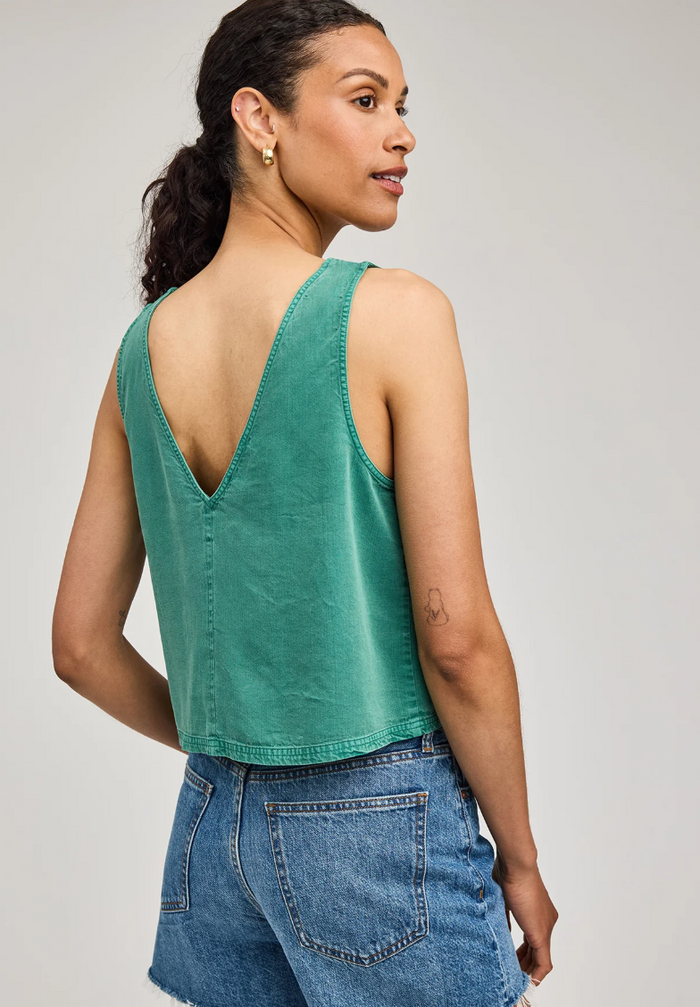 Woman wearing a green tank top and blue jeans on a plain background