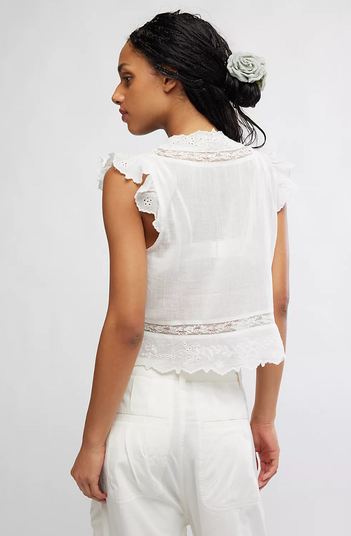 Woman wearing a ivory lace top and pants against a plain background