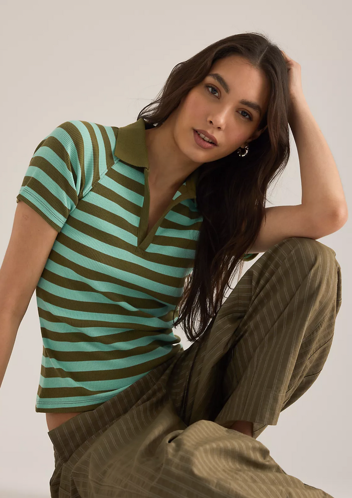 Woman wearing a striped polo shirt and pants against a plain background