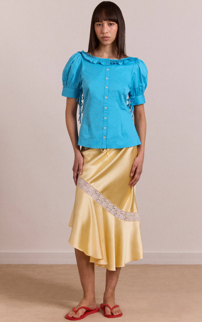Woman wearing a blue top and yellow skirt with lace trim against a beige background