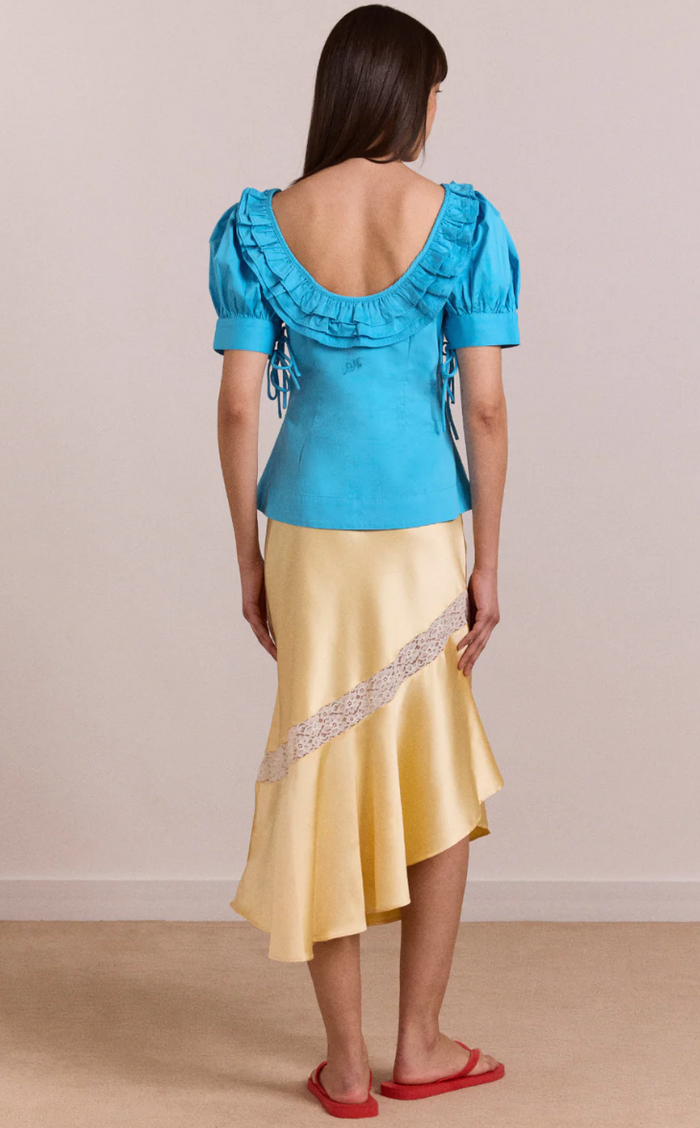 Woman wearing a blue top and yellow skirt with a beige background