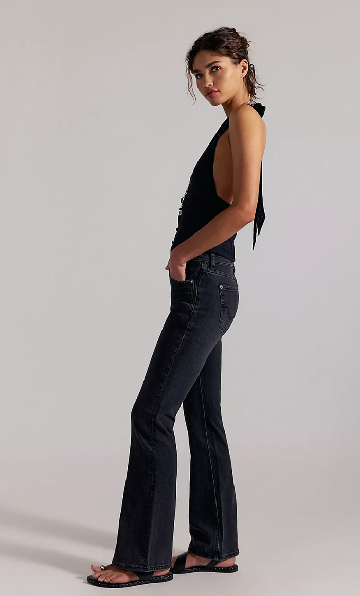 Woman wearing dark horizon flared jeans and a black top on a plain background