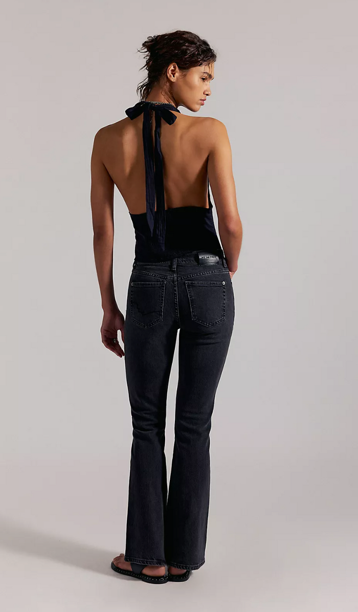 Woman wearing a black open-back top and flared jeans on a plain background