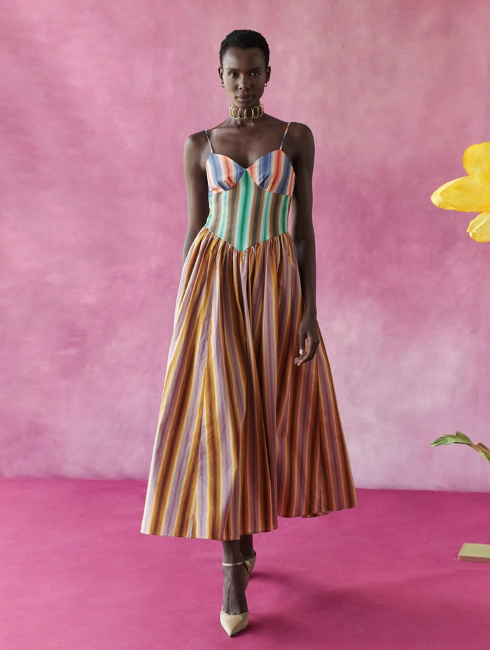 Model wearing a colorful striped dress against a pink background