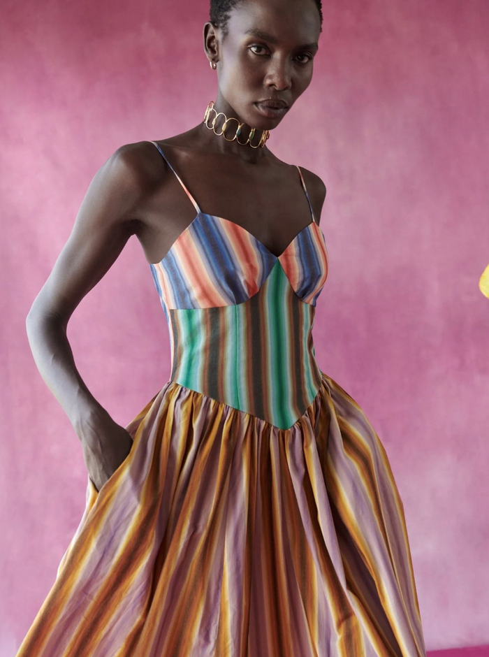 Woman wearing a colorful striped dress against a pink background