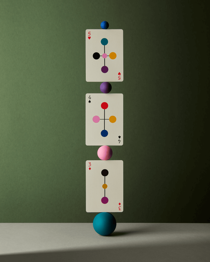 Three playing cards with colorful symbols balanced on a blue sphere against a green background