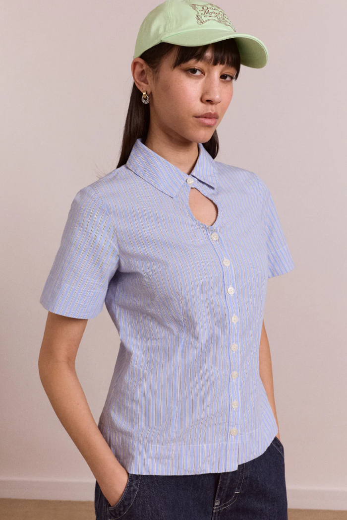 Person wearing a light blue striped shirt and green cap against a plain background