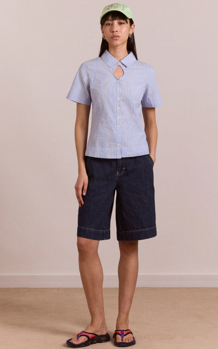 Person wearing a light blue checkered shirt and dark blue shorts against a beige background