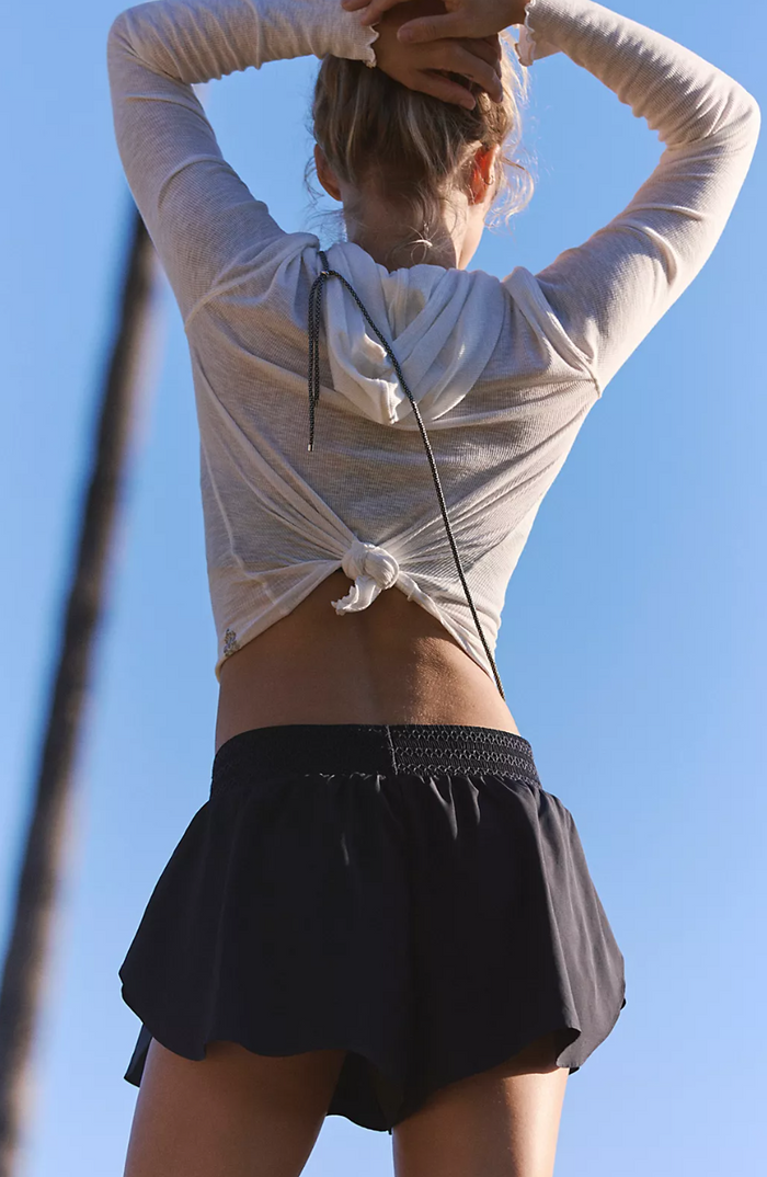 Person wearing a light-colored long-sleeve top and black shorts against a clear blue sky.