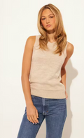 Woman wearing a beige sleeveless top and blue jeans against a white background
