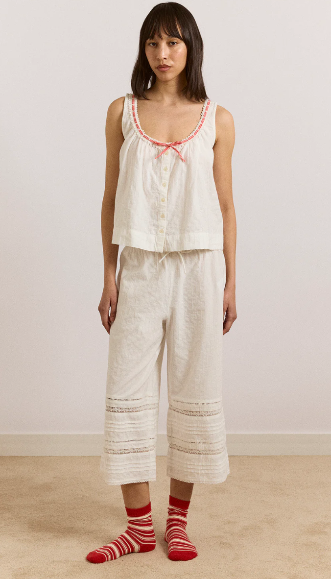 Woman wearing a white sleeveless top and pants with red striped socks on a plain background