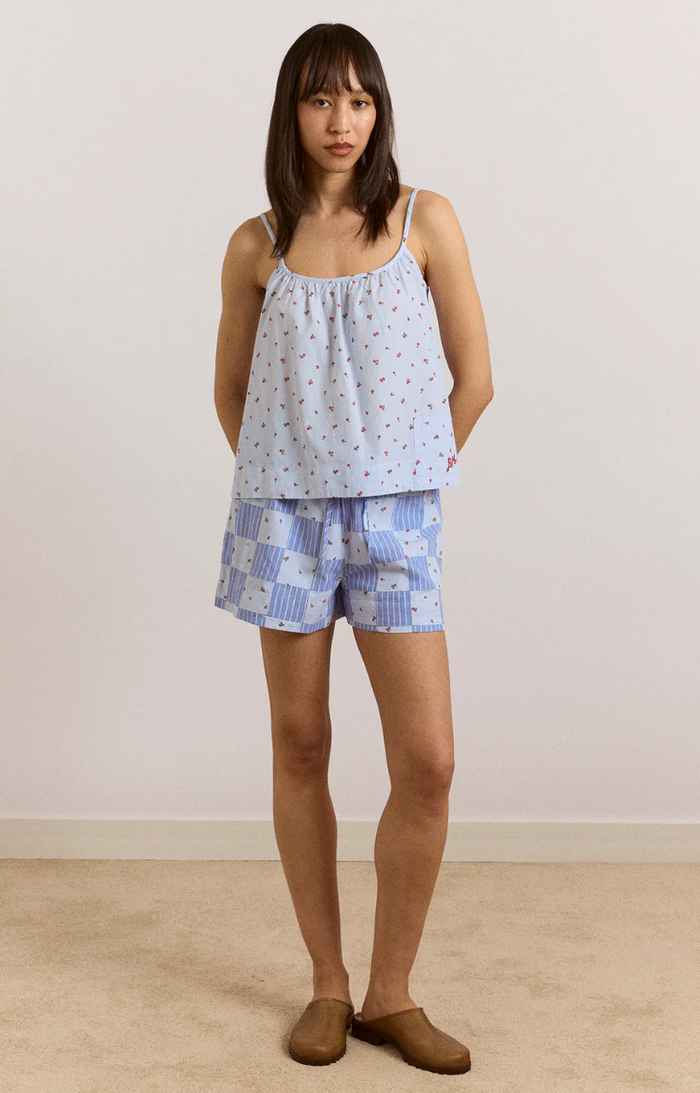 Woman wearing a light blue pajama top and checkered shorts against a plain background