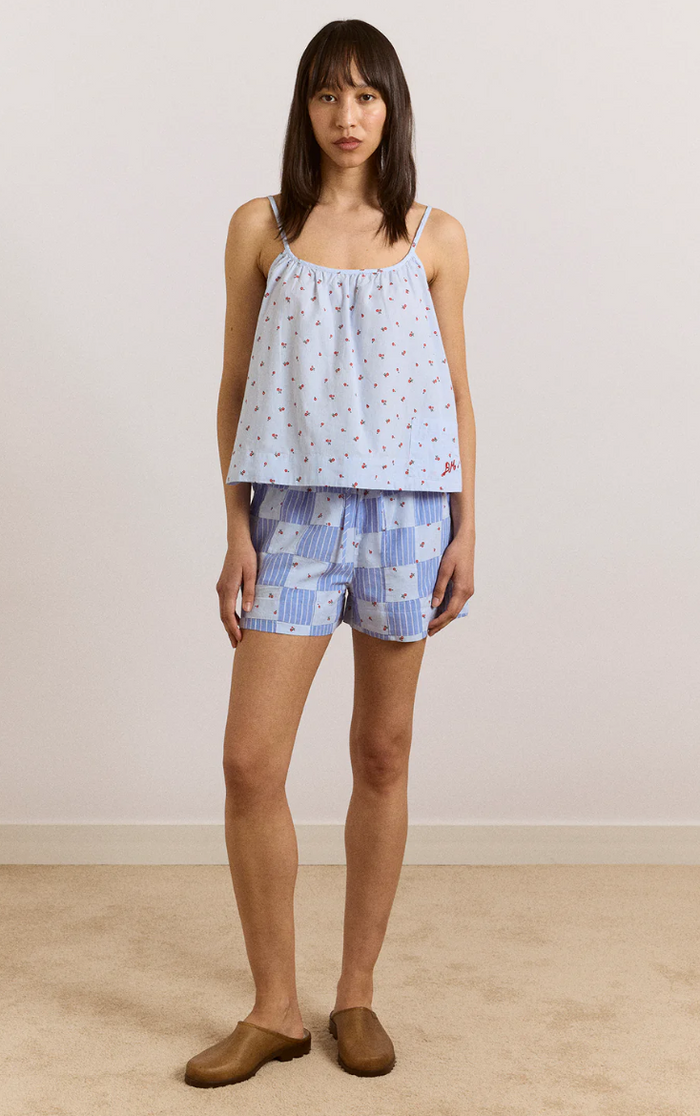 Woman wearing a light blue patterned top and checkered shorts on a plain background