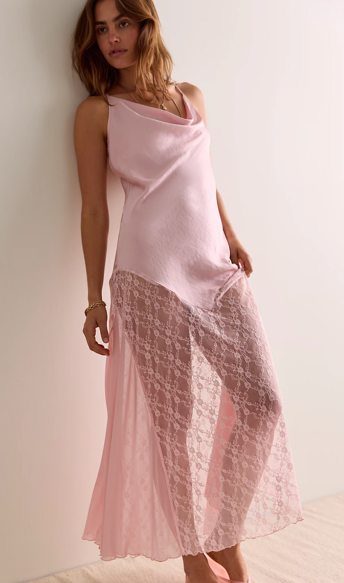 Woman wearing a light pink sleeveless top and lace skirt against a plain background