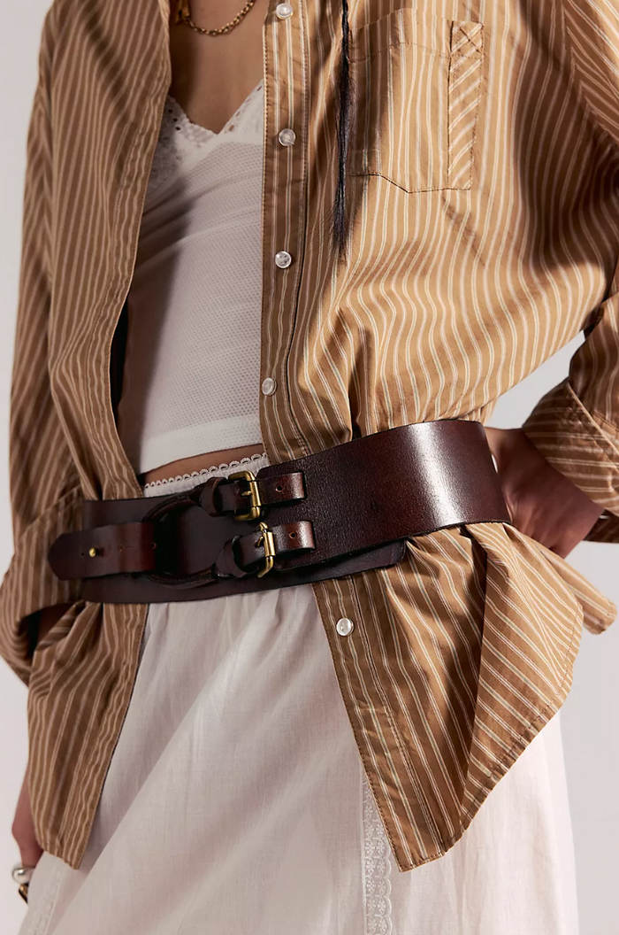 Person wearing a brown striped shirt with a white dress underneath, accentuated by a Free People Everhart Hip Belt in Espresso.