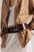 Person wearing a brown striped shirt with a white dress underneath, accentuated by a Free People Everhart Hip Belt in Espresso.