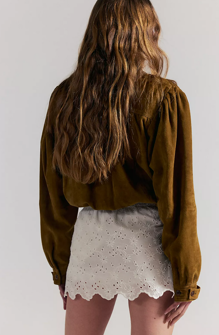 Woman wearing an olive green jacket and ivory lace skort on a white background