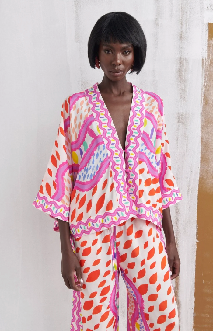 A model wearing a matching two-piece lounge set featuring a white base with orange, pink, and blue abstract patterns and wavy pink borders.