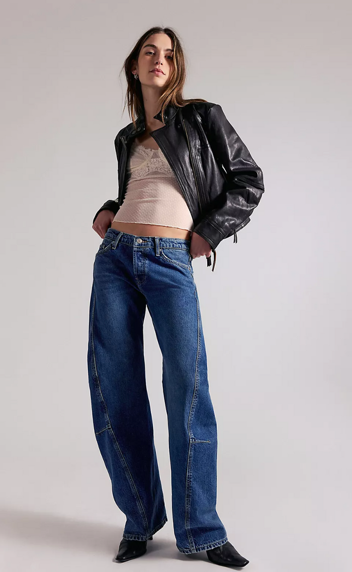 Woman wearing a black leather jacket and blue jeans on a plain background