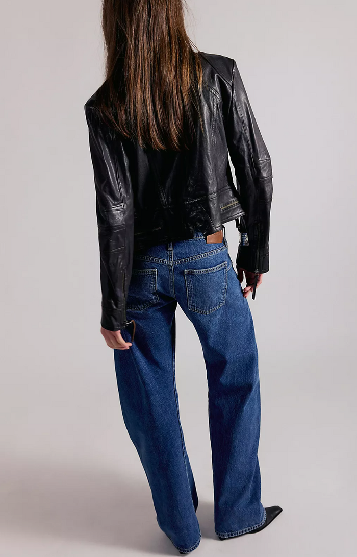 Person wearing a black leather jacket and blue jeans on a plain background