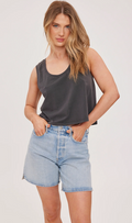 Woman wearing a dark gray tank top and light blue denim shorts on a plain background